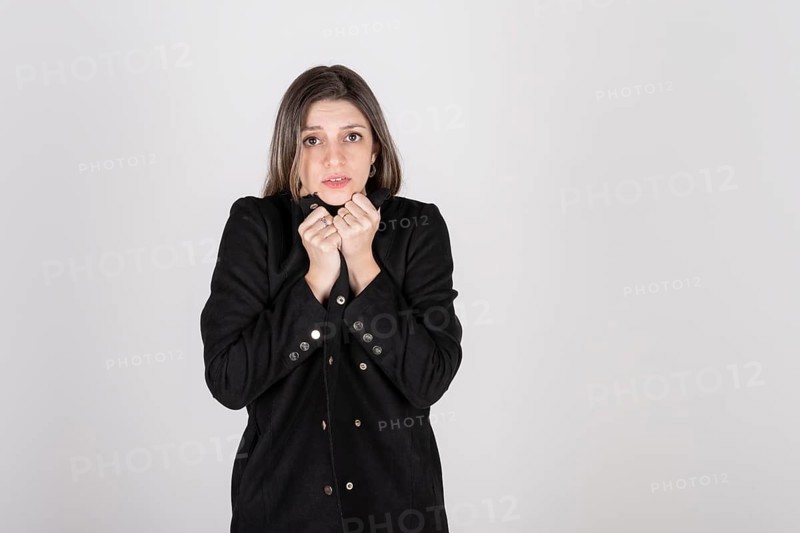Studio portrait of young blonde woman wearing a black coat with expression of cold and disgust