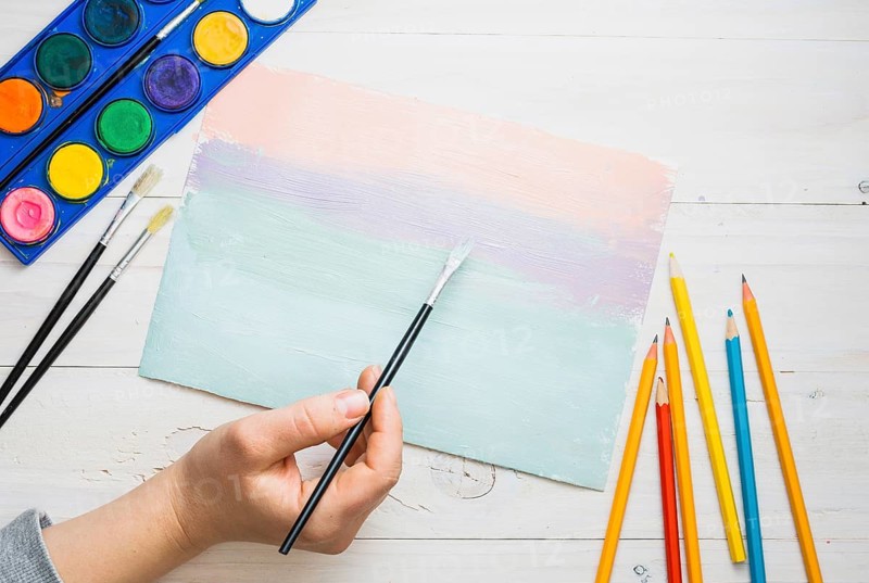 Person s hand painting paper with paint brush watercolor desk