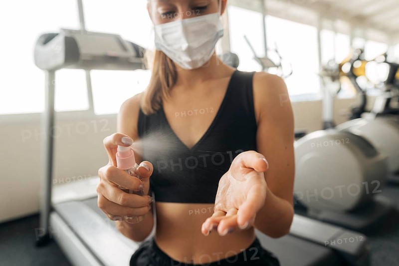 Woman with medical mask gym using hand sanitizer