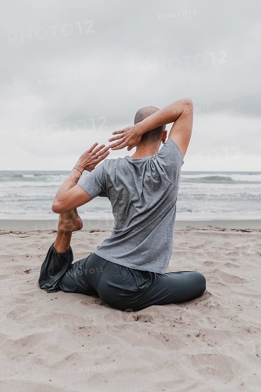 Back view man beach exercising yoga