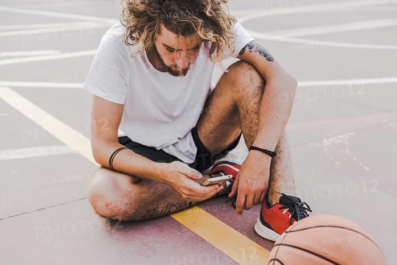 Basketball player sitting court using mobile phone