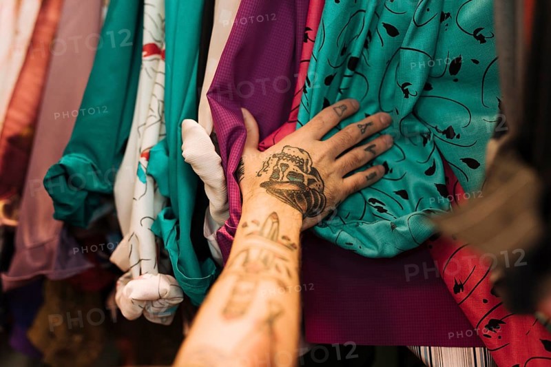 Close up man with tattoo his hand touching shirts arranged rail