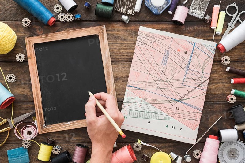 Crop hand drawing blackboard near sewing stuff