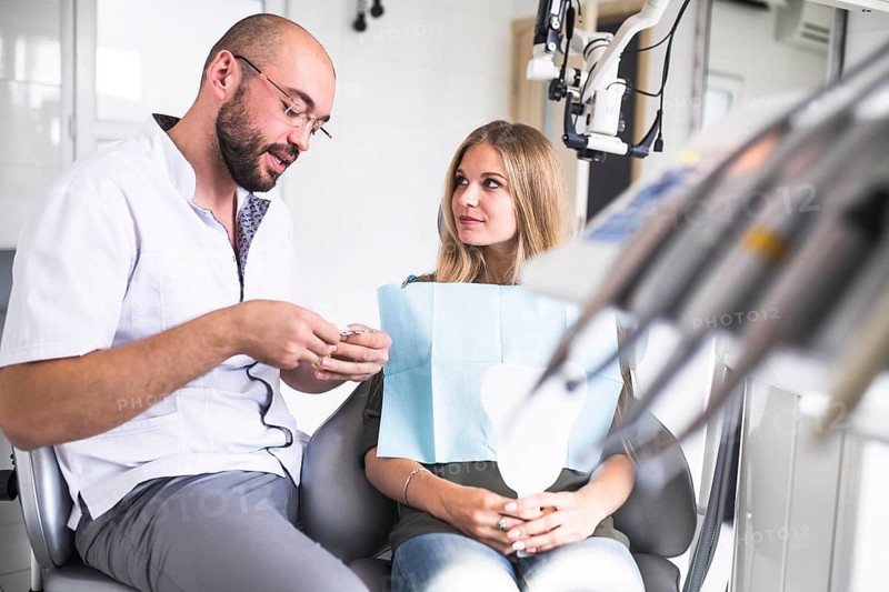 Dentist talking with female patient while working dental jaw