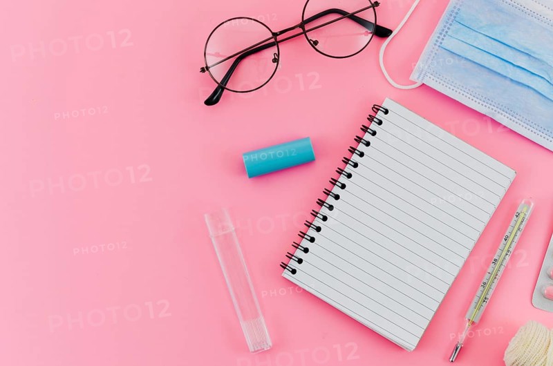 Eyeglasses thermometer surgical mask spiral notebook pink background