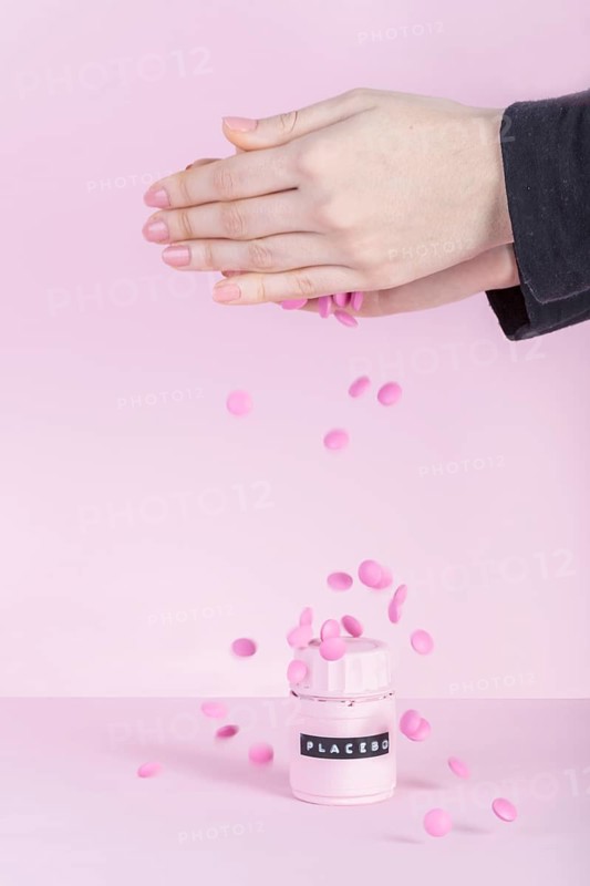 Female s hand falling pink pills placebo bottle pink background