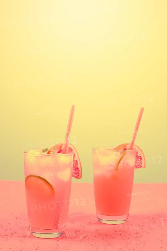 Fresh pink alcoholic cocktail with grapefruit lemon slice ice cubes against yellow background