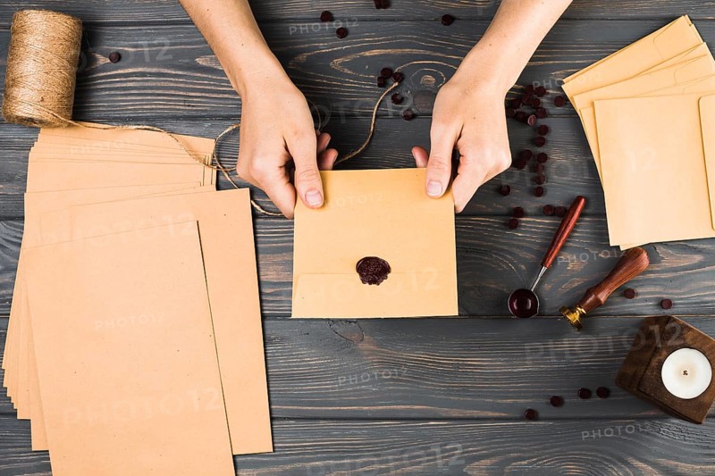 High angle view woman showing seal brown envelop with craft material wooden table