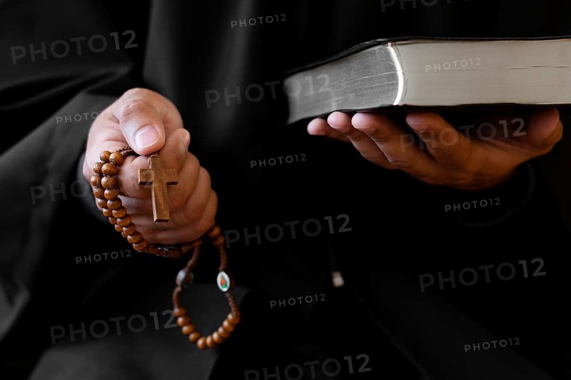 Person holding rosary with cross holy book