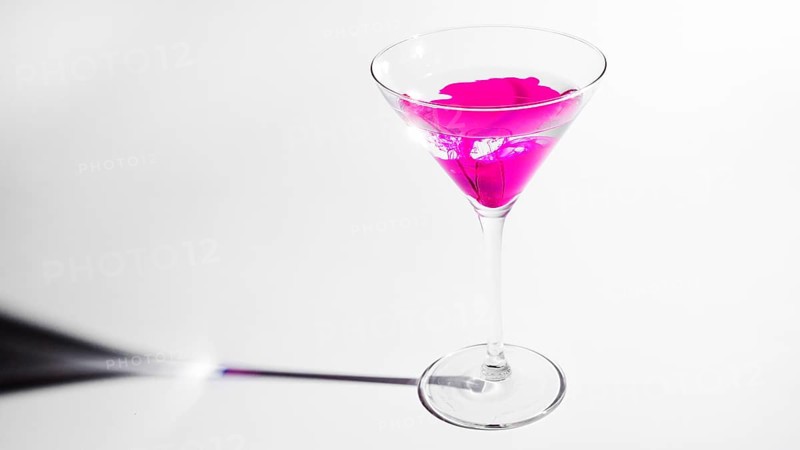 Pink ink dissolving martini glass isolated white backdrop