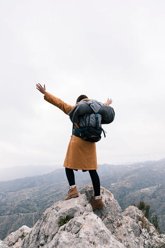 Rear view woman raising her arms standing top mountain
