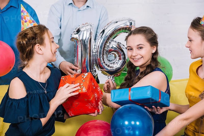 Smiling portrait birthday girl with number 16 foil balloon presents
