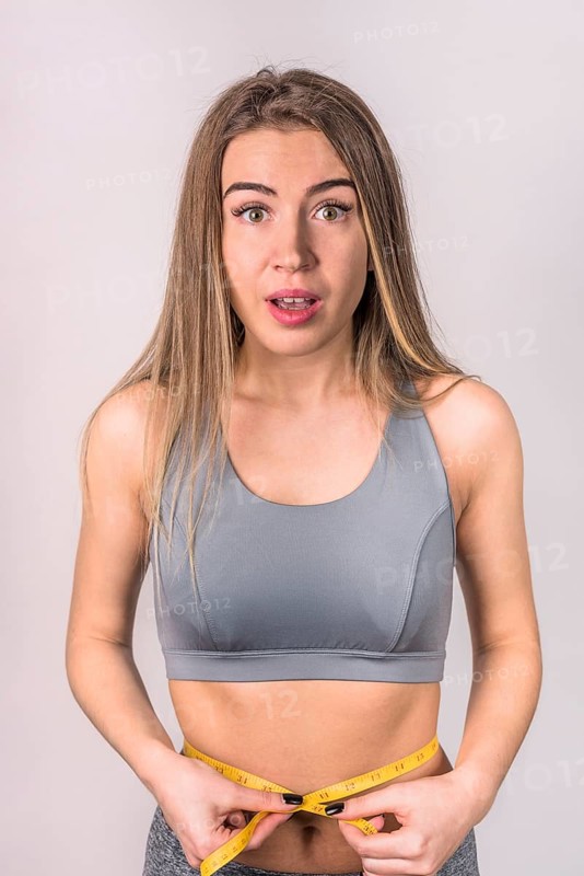 Surprised attractive slim woman measuring waist