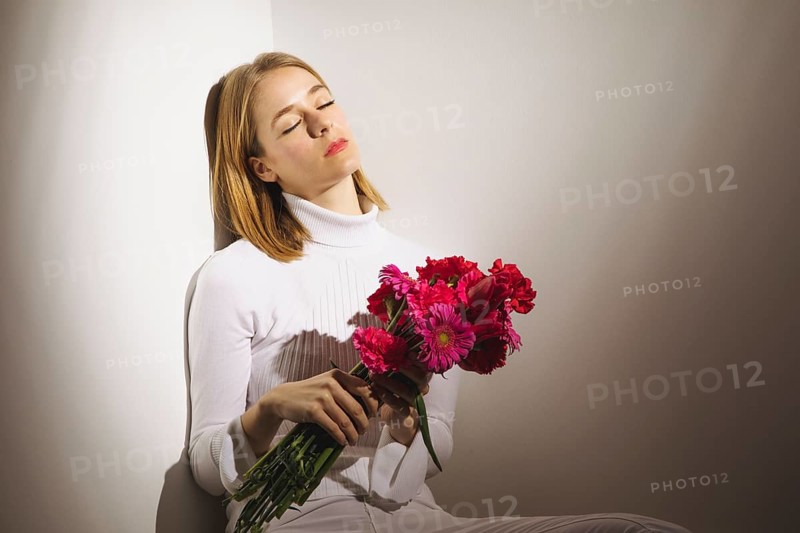 Thoughtful woman sitting with pink flowers bouquet