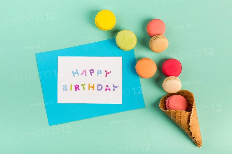 Waffle cone with macaroons near happy birthday card mint green backdrop