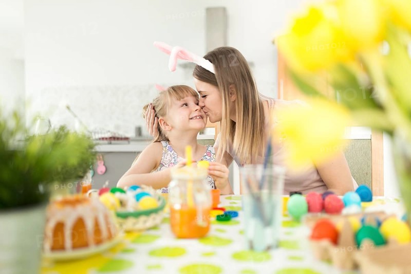 Woman kissing daughter decorating easter eggs