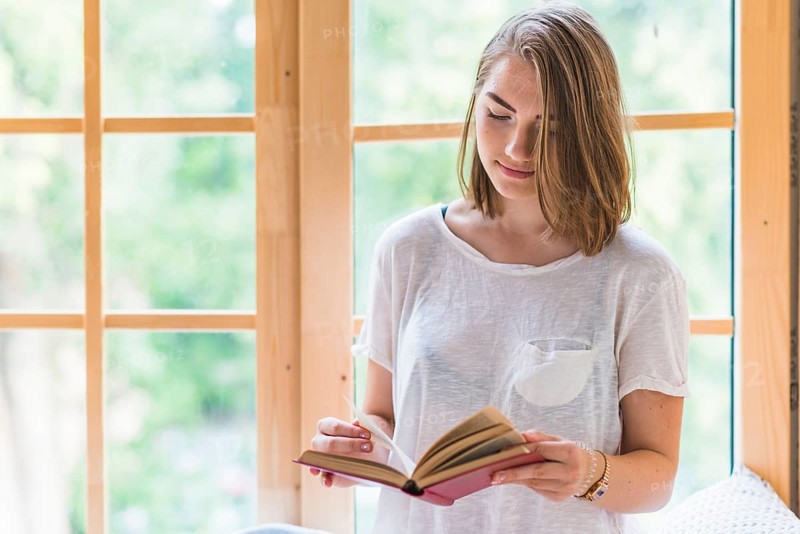 Woman standing front window reading book