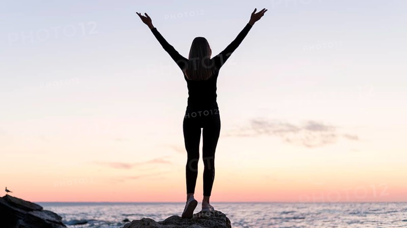 Back view woman standing coast with her arms up