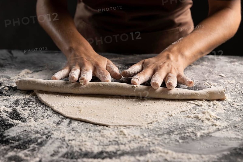 Chef rolling dough with lot flour table