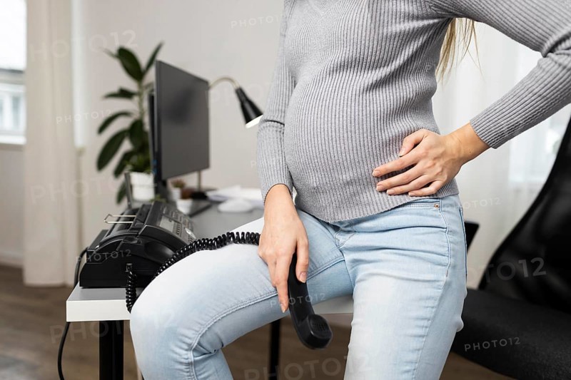 Side view pregnant businesswoman sitting desk holding phone receiver
