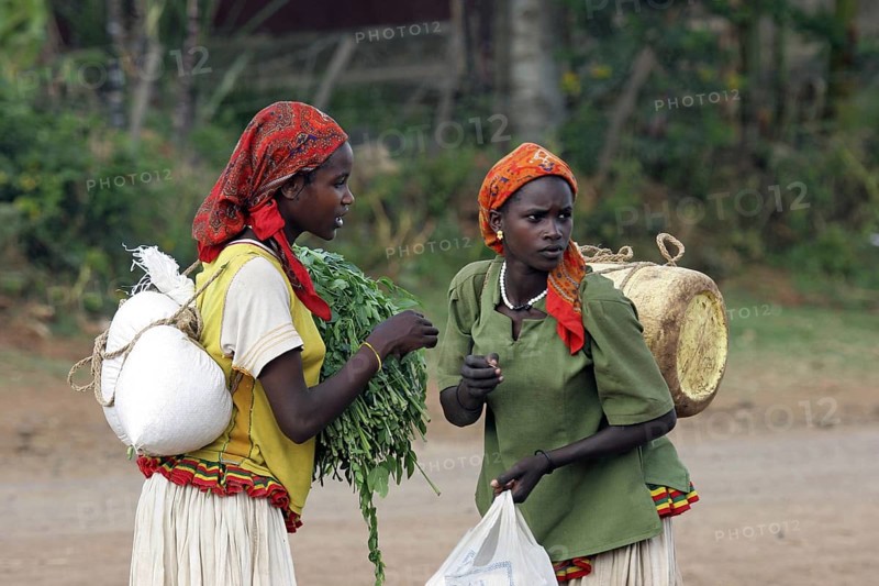Two young women carrying merchandise on their back in street in Konso