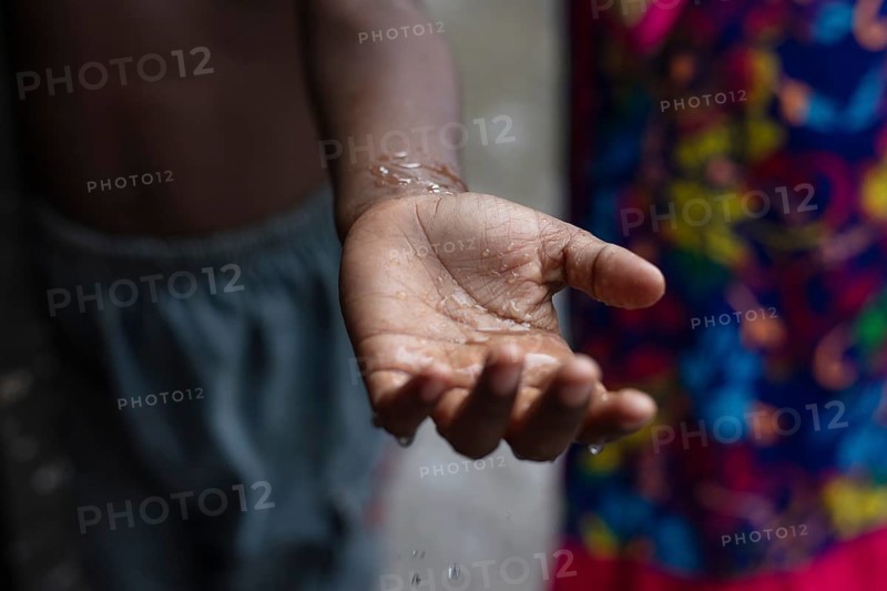 Drops of water fall on the palm of a boy's hand during a monsoon downpour