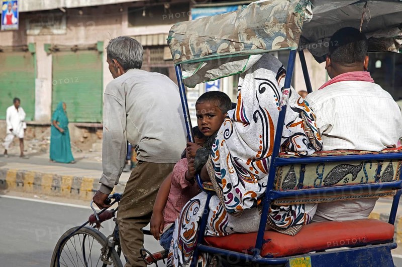 Cycle rickshaw with old driver transporting family as urban transport in Mathura