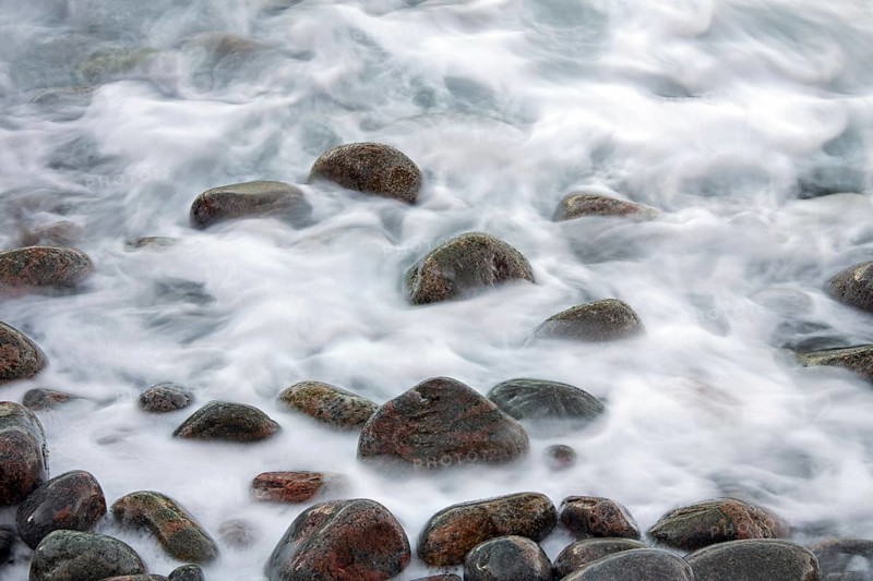 Close up of colourful cobbles covered by wave on shingle beach at rising tide