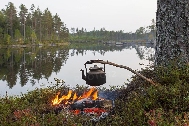 Blackened tin kettle boiling water over flames from campfire during hike along lake