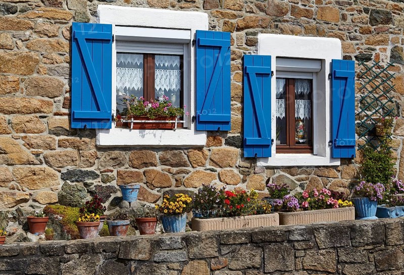 Windows with blue shutters and colourful flowers in front of a natural stone facade in Paimpol