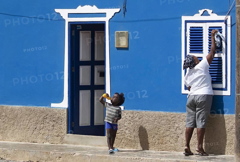 Child and mother cleaning window shutters of blue coloured house in the village Bofareira