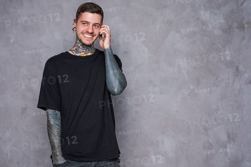 Smiling portrait tattooed young man with pierced ears talking mobile phone