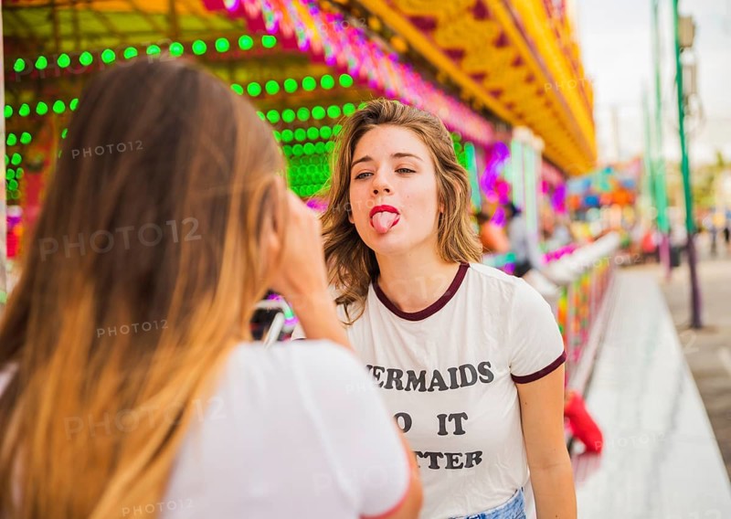 Rear view woman taking her friend showing tongue amusement park