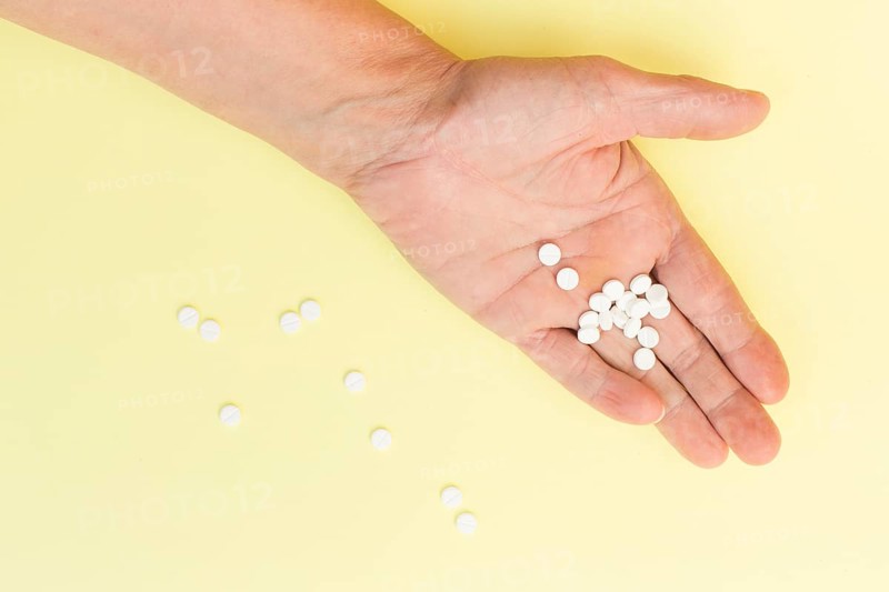 White round tablets hand person against yellow background