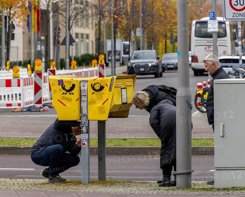 Tourists marvelling at and examining a yellow letterbox by the roadside