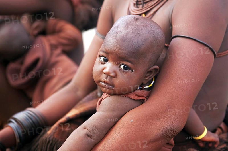 Close up of baby in mother's arms of the Himba tribe with red skin covered in otjize