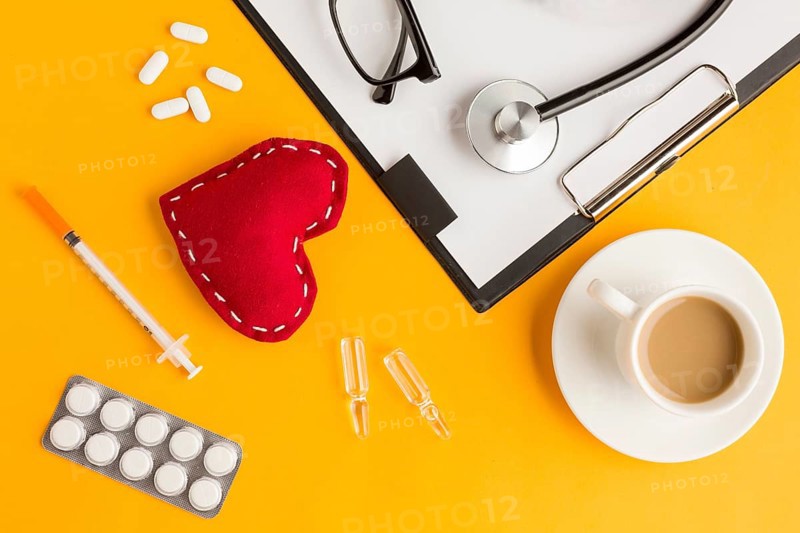 Red stitched heart coffee cup stethoscope eyeglass injection blister packed medicine clipboard against yellow backdrop