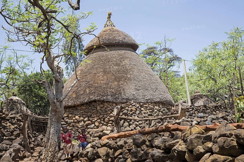 Two black children in front of traditional stone hut with thatched roof of the Konso