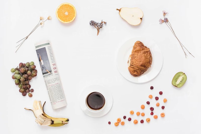 Rolled up newspaper with coffee cup croissant fruits white background