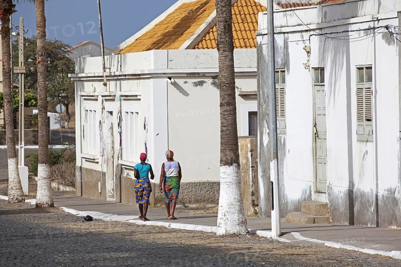 Local Creole women walking in street along white colonial buildings of the town Tarrafal on the island Santiago