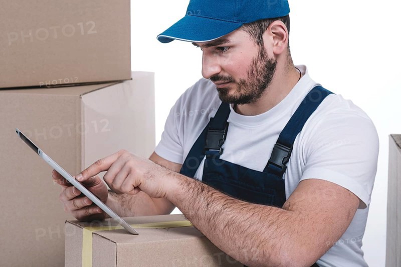Serious courier browsing tablet near parcels
