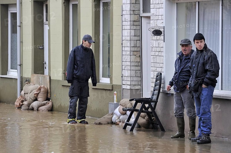 Flooded street and sandbags piled up in front of doors at Nederzwalm