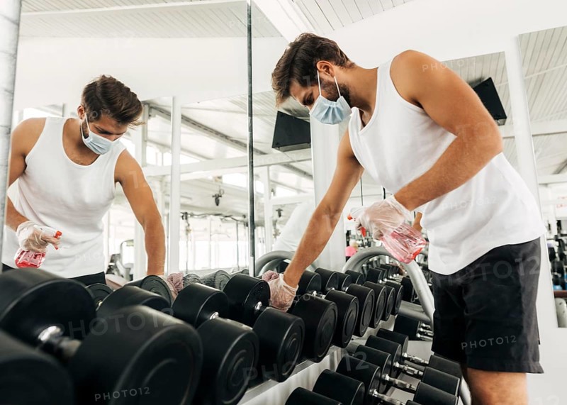 Side view man disinfecting gym equipment while wearing medical mask