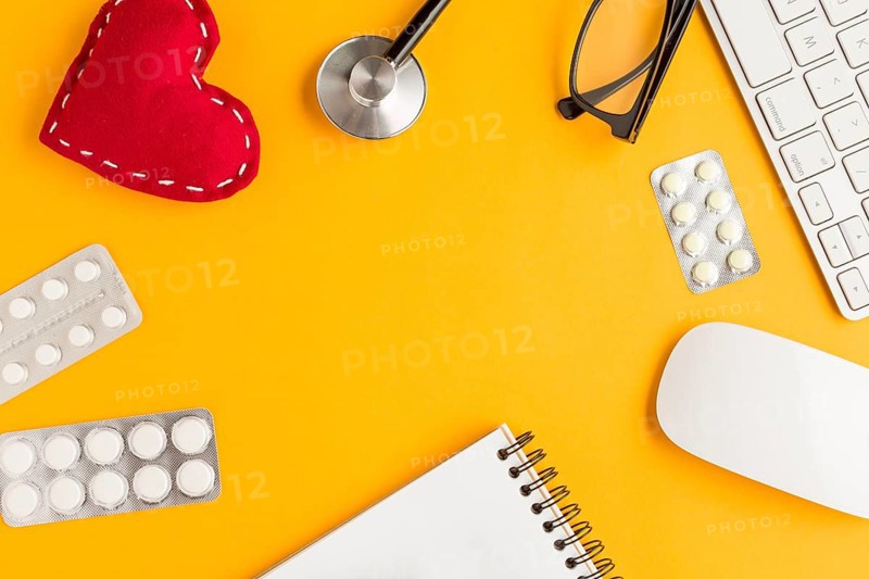 Arrangement blister packed medicines stitched heart shape spiral notepad wireless keyboard mouse spectacles stethoscope yellow backdrop