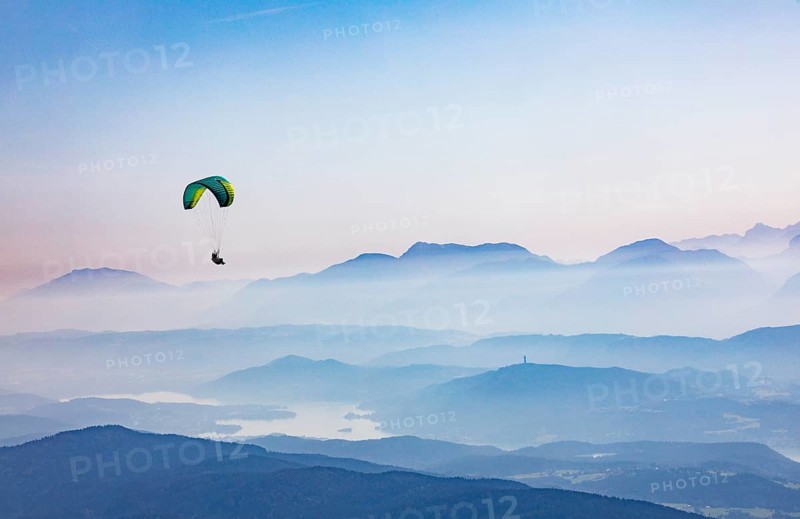Paragliders high above the mountains with a view of the Klagenfurt basin and the Karawanken