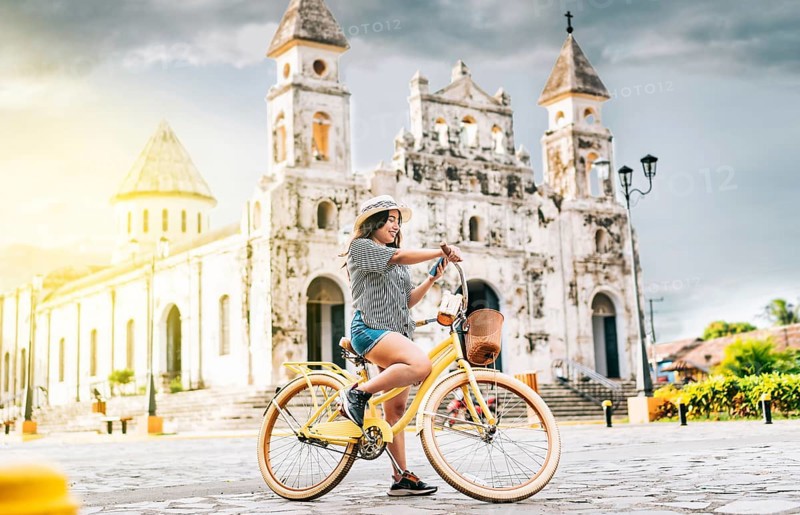 The girl is on the street smiling at the cell phone while she is on her bicycle