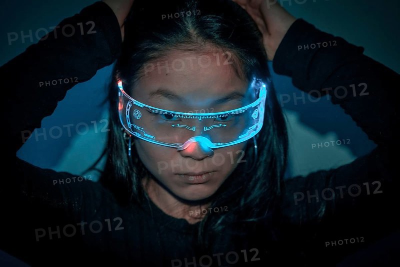 Close-up studio photo with blue background with neon lights of a chinese young woman using augmented reality goggles