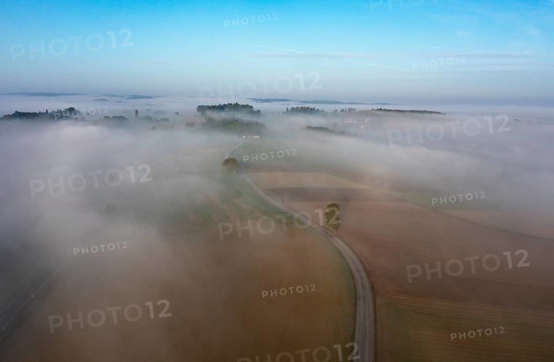 Drone view of a rural landscape shrouded in dense morning fog with a country road near Prambachkirchen