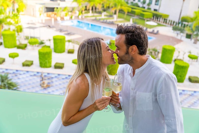 Newlywed couple kissing while toasting with champagne in the terrace of a luxury hotel