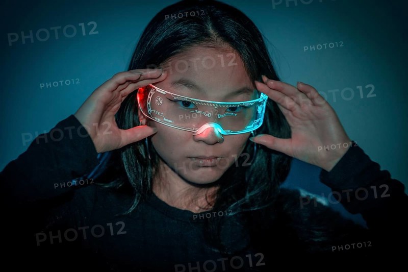 Studio photo with blue background with neon lights of a chinese woman with cybernetic glasses looking at camera